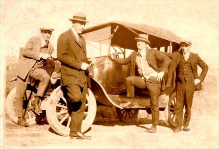 A group of men standing next to an old fashioned car.