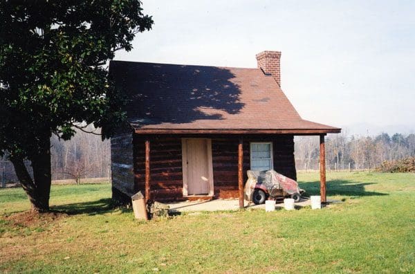 A log cabin with a porch and an old car parked in front of it.