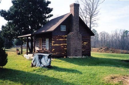 A log cabin with a cow in the yard.