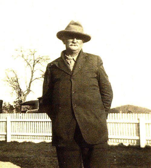 A man in a hat and coat standing next to a fence.