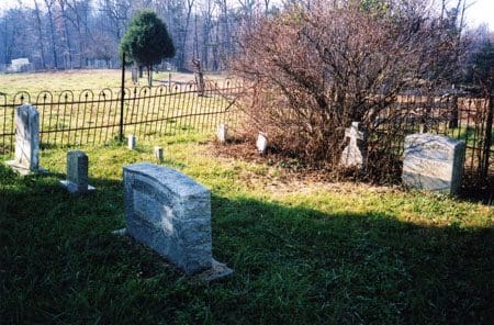 A cemetery with a tree and fence in the background.