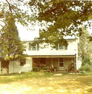 An old photo of a house with a lawn and trees.