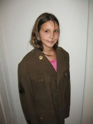 A girl in military uniform standing next to a wall.