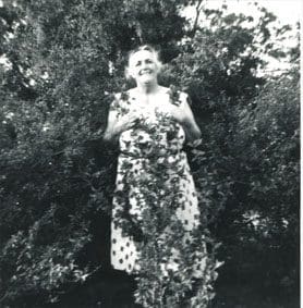 A woman standing in front of trees holding flowers.