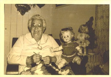 An old woman and a doll are sitting in a chair.