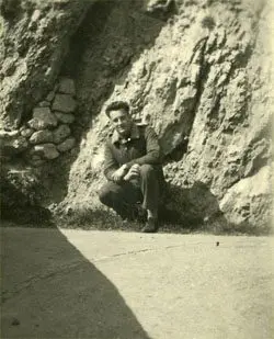 A man sitting on the ground in front of a rock wall.