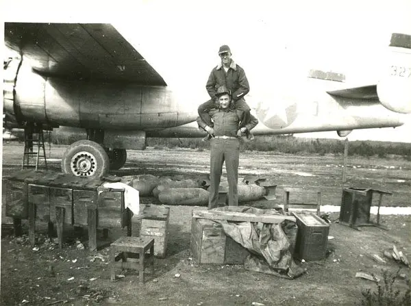 A man standing on the back of another man in front of an airplane.