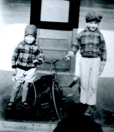 Two young boys standing next to a bicycle.