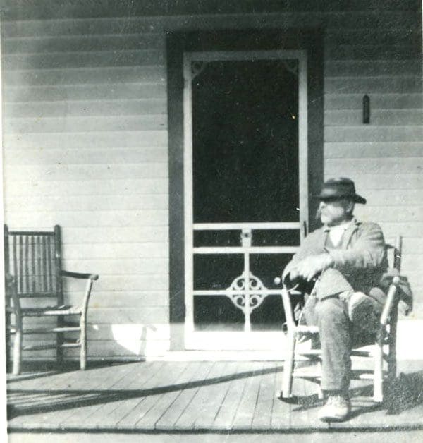 A man sitting on a rocking chair outside of a house.