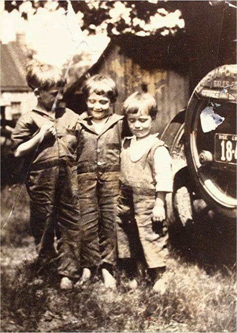 Three boys standing in front of a car.