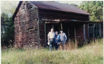 Three people standing in front of a dilapidated house.