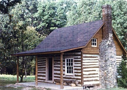 A log cabin with a stone wall and trees in the background.