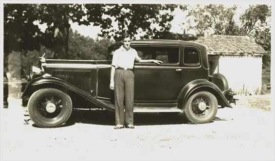 An old photo of a man standing next to a car.