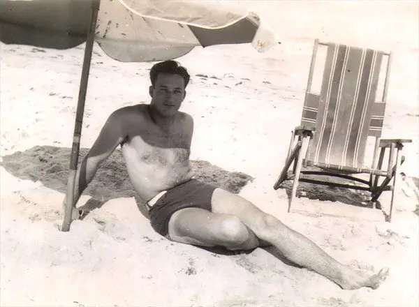 A man sitting on the beach under an umbrella.