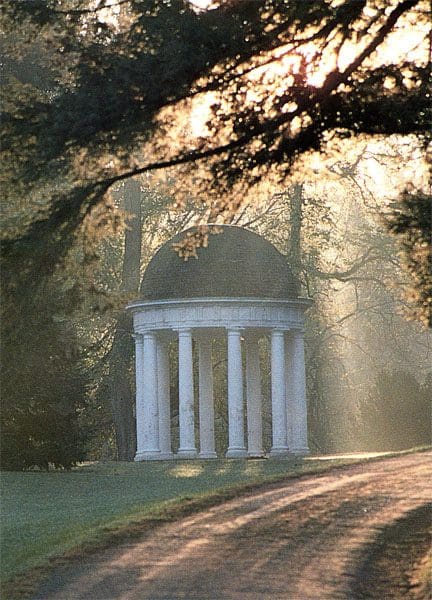 A white building with pillars in the middle of a park.