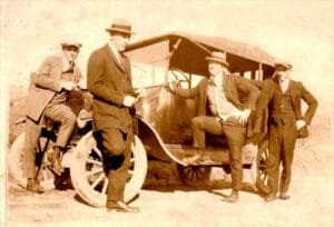 A group of men standing next to an old fashioned car.