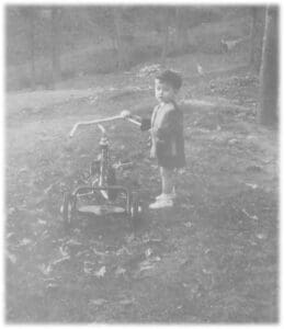 A young boy standing next to a tricycle.