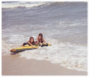 Two girls laying on a surfboard in the ocean.