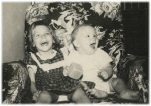 Two children sitting on a chair laughing.