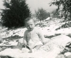 A baby sitting in the snow on top of a blanket.