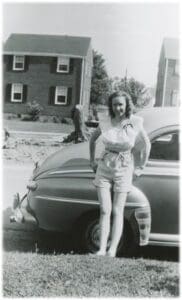 A woman standing next to an old car.