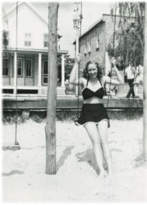 A woman in black bathing suit standing on sand.