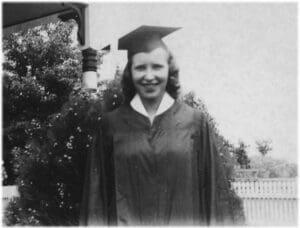 A woman in graduation gown and cap standing next to a tree.