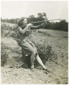 A woman sitting on the ground holding a rifle.