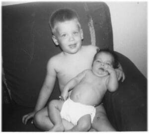 A young boy and baby sitting on the couch.