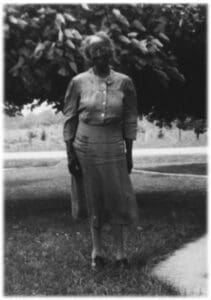 A woman standing in the grass near a tree.