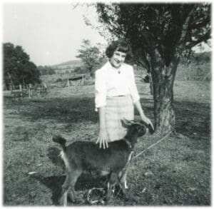 A woman standing next to a goat in the grass.