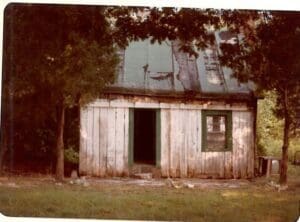 A dilapidated house with a green door and window.