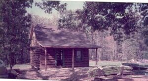 A log cabin with a porch and trees in the background.