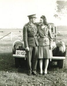 A man and woman standing next to an old car.