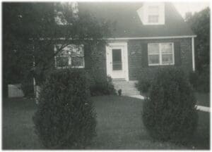 A black and white photo of a house with bushes in front.