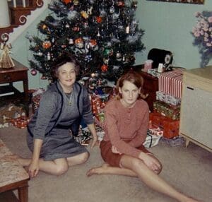 Two women sitting in front of a christmas tree.