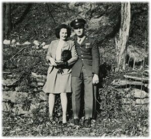 A man and woman standing in the woods.