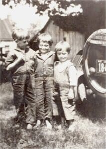 Three boys standing in front of a car.