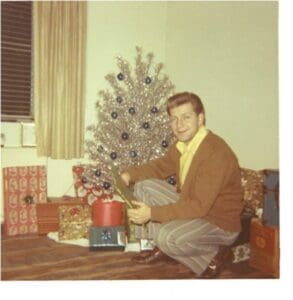 A man sitting in front of a christmas tree.